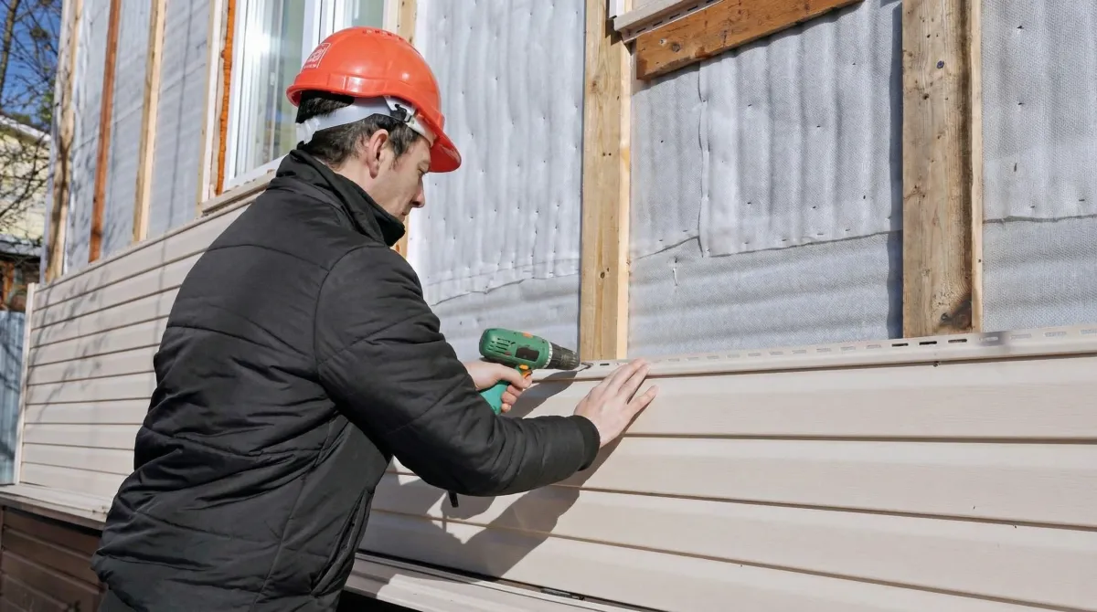 Siding replacement professional using a power drill to install new tan vinyl siding on a home exterior in Tallahassee, FL